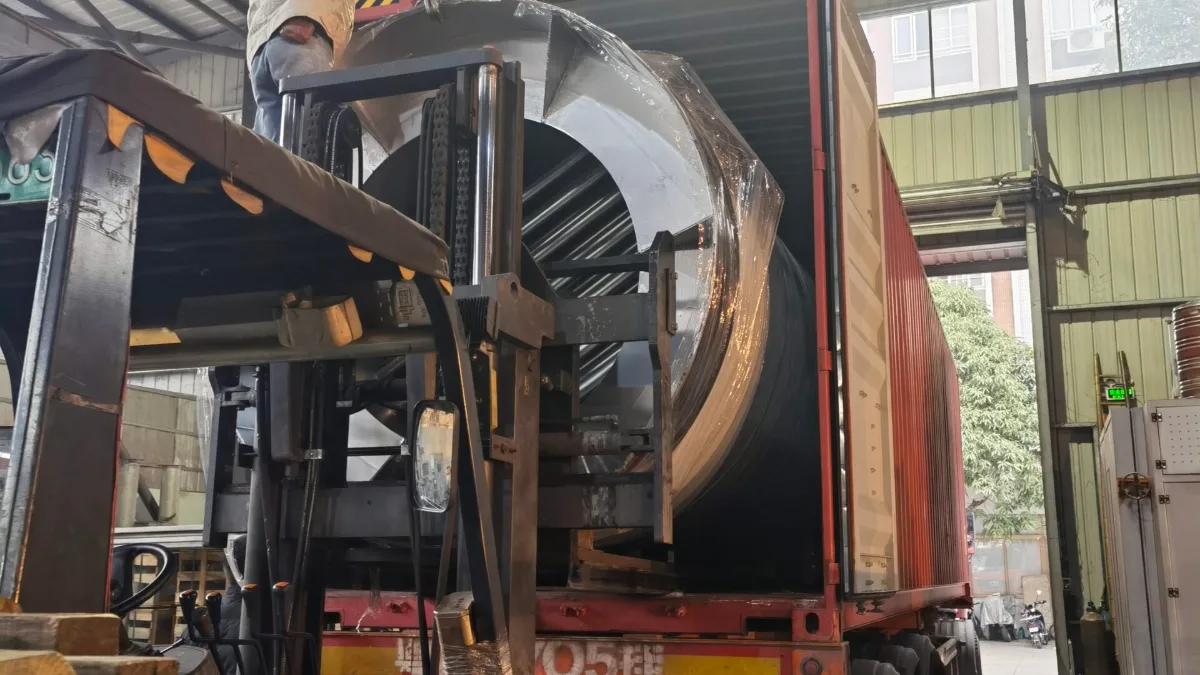Forklift loading a large steel drum into a container at a factory