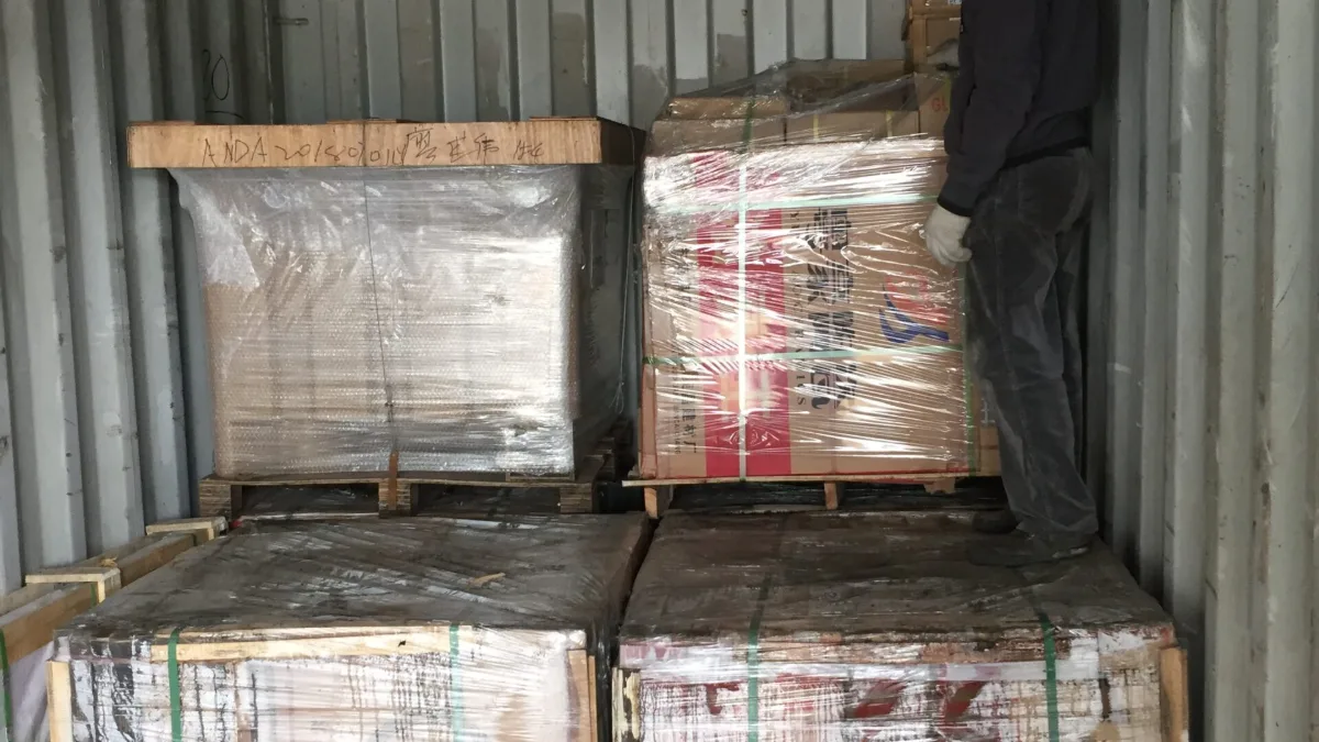 Worker checking stretch-wrapped pallets inside a container
