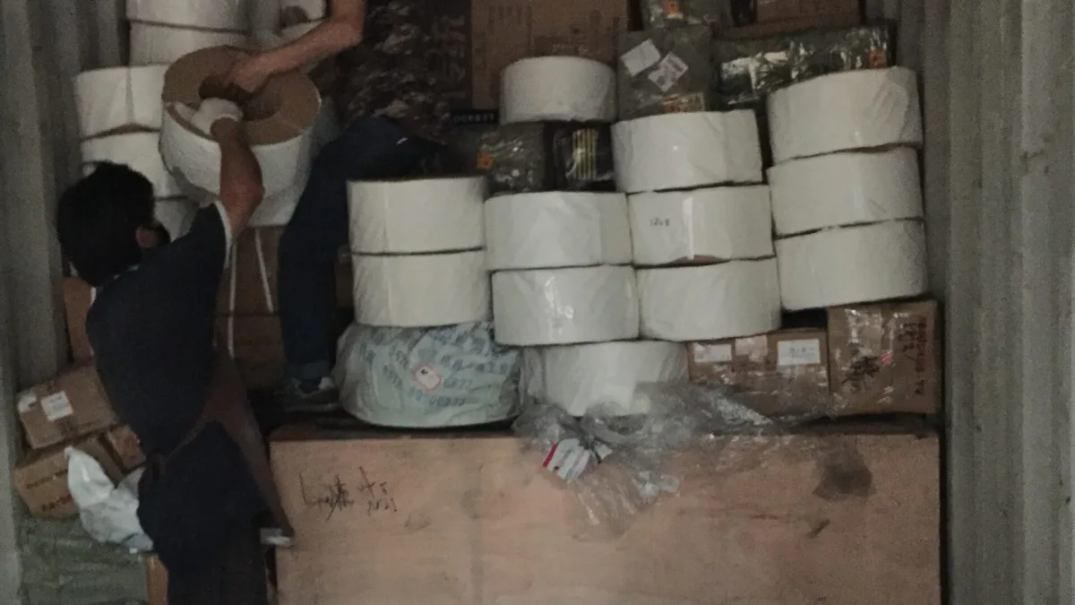 Workers loading rolls and cartons into a shipping container